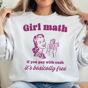 May include: White sweatshirt with a pink graphic of a woman holding money and the text "Girl math if you pay with cash it's basically free".