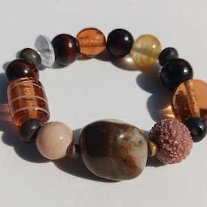 May include: A multi-coloured beaded bracelet. The bracelet features a mix of brown, orange, clear, and pink beads. The beads are different shapes and sizes, creating a unique accessory. The bracelet is suitable for everyday wear.