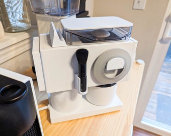May include: White coffee maker with a clear top and a black brush attached to the side. The coffee maker has a white base and a silver ring around the top. The brush is labeled "Fellow".