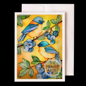May include: Watercolor art greeting card featuring two bluebirds perched on a branch with blueberries. The birds have blue and orange feathers, set against a yellow background. The card includes a white envelope and the text "THE PRAIRIE ARTIST" in a circular logo.