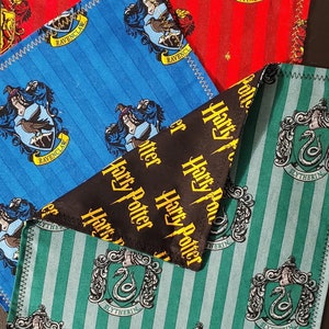 May include: Four fabric squares with Harry Potter house crests. The squares are blue with a raven, red with a lion, green with a snake, and black with the words "Harry Potter" repeated. The squares are sewn together with a zig-zag stitch.