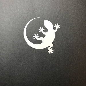 May include: A white silhouette of a gecko curled in a circle on a black background.