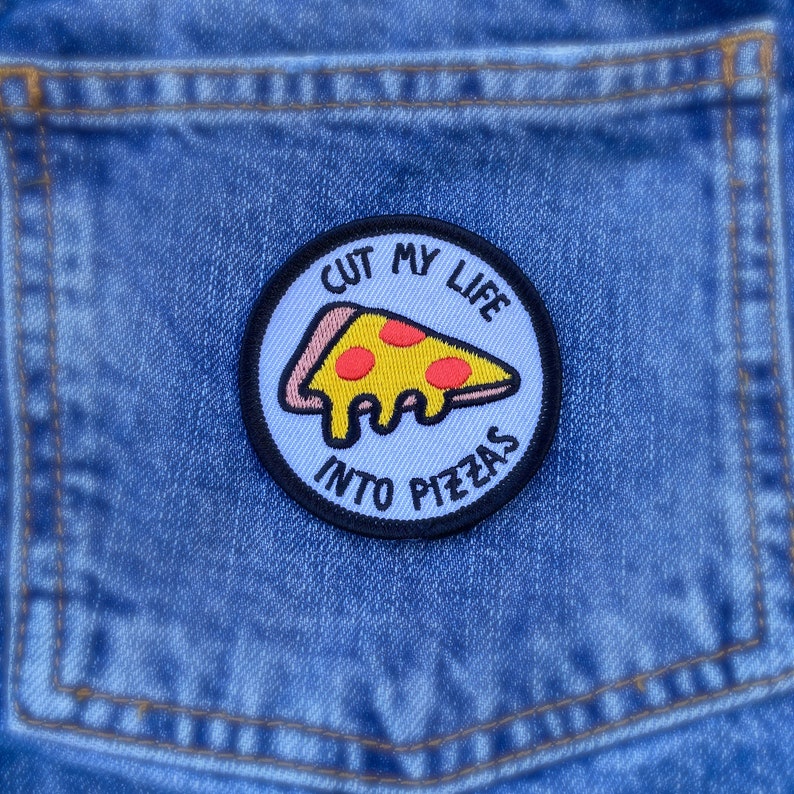 May include: A blue denim jean pocket with a white and black embroidered patch that says "Cut my life into pizzas" with a yellow and red pizza slice inside.