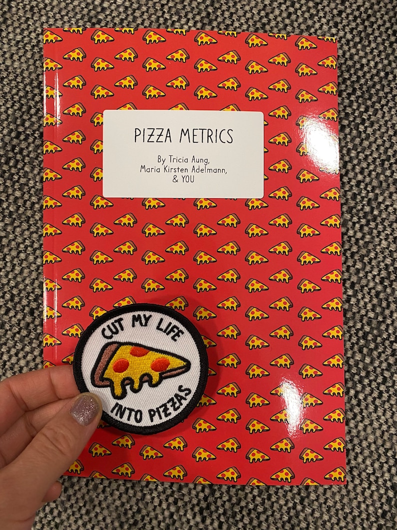 May include: A red book with a pizza pattern on the cover. The book title is "Pizza Metrics" and the authors are Tricia Aung, Maria Kirsten Adelmann, and "You". A white patch with a pizza slice and the text "Cut my life into pizzas" is attached to the front cover.