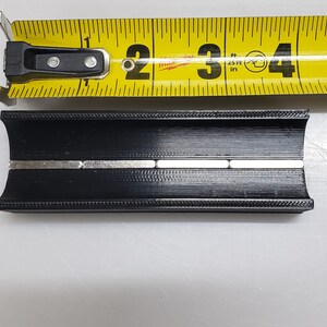 May include: A black plastic channel with a row of silver magnets embedded in the centre. The channel is approximately 7.6 cm long.