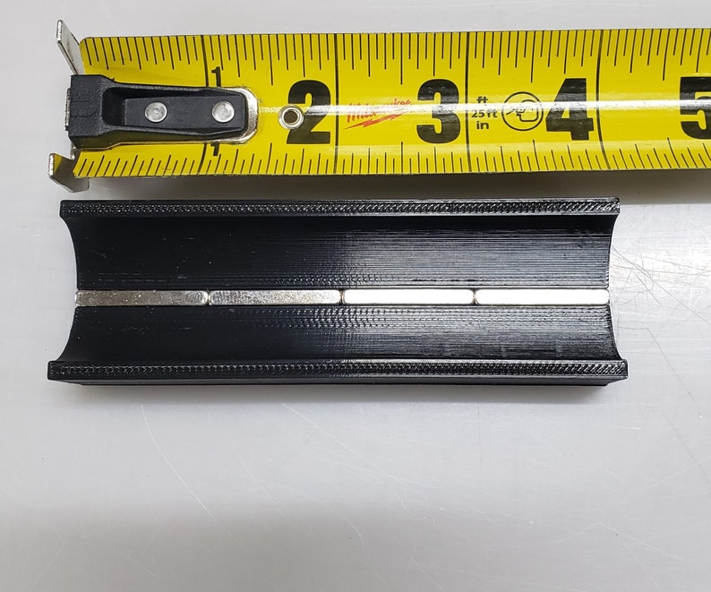 May include: A black plastic channel with a row of silver magnets embedded in the centre. The channel is approximately 7.6 cm long.