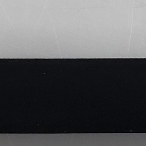 May include: A black rectangular strip of material is measured with a yellow tape measure. The tape measure reads 1 inch.