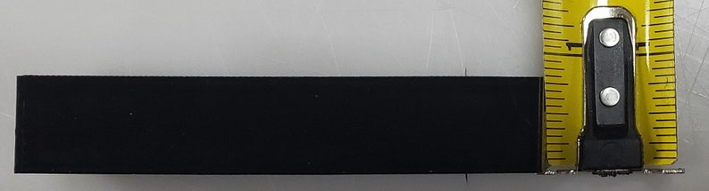 May include: A black rectangular strip of material is measured with a yellow tape measure. The tape measure reads 1 inch.
