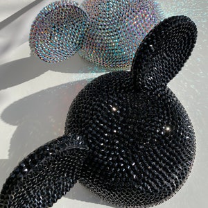 May include: Two pairs of Mickey Mouse ears, one black and one iridescent. The ears are covered in rhinestones.
