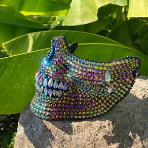Pu&ograve; includere: Una maschera di teschio nera ricoperta di strass iridescenti. La maschera ha un design dettagliato con una grande bocca aperta e denti affilati.
