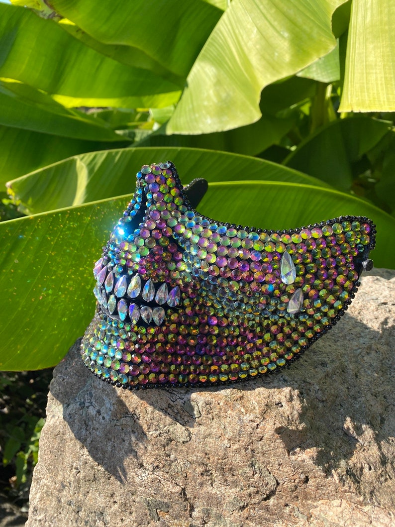Pu&ograve; includere: Una maschera di teschio nera ricoperta di strass iridescenti. La maschera ha un design dettagliato con una grande bocca aperta e denti affilati.