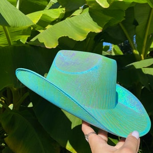 May include: A turquoise blue cowboy hat with a iridescent finish. The hat has a wide brim and a pointed crown.