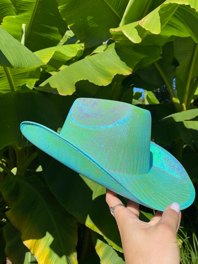 May include: A turquoise blue cowboy hat with a iridescent finish. The hat has a wide brim and a pointed crown.