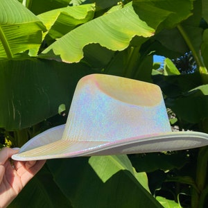 May include: A white iridescent cowboy hat with a wide brim. The hat is made of a shiny material that reflects light.
