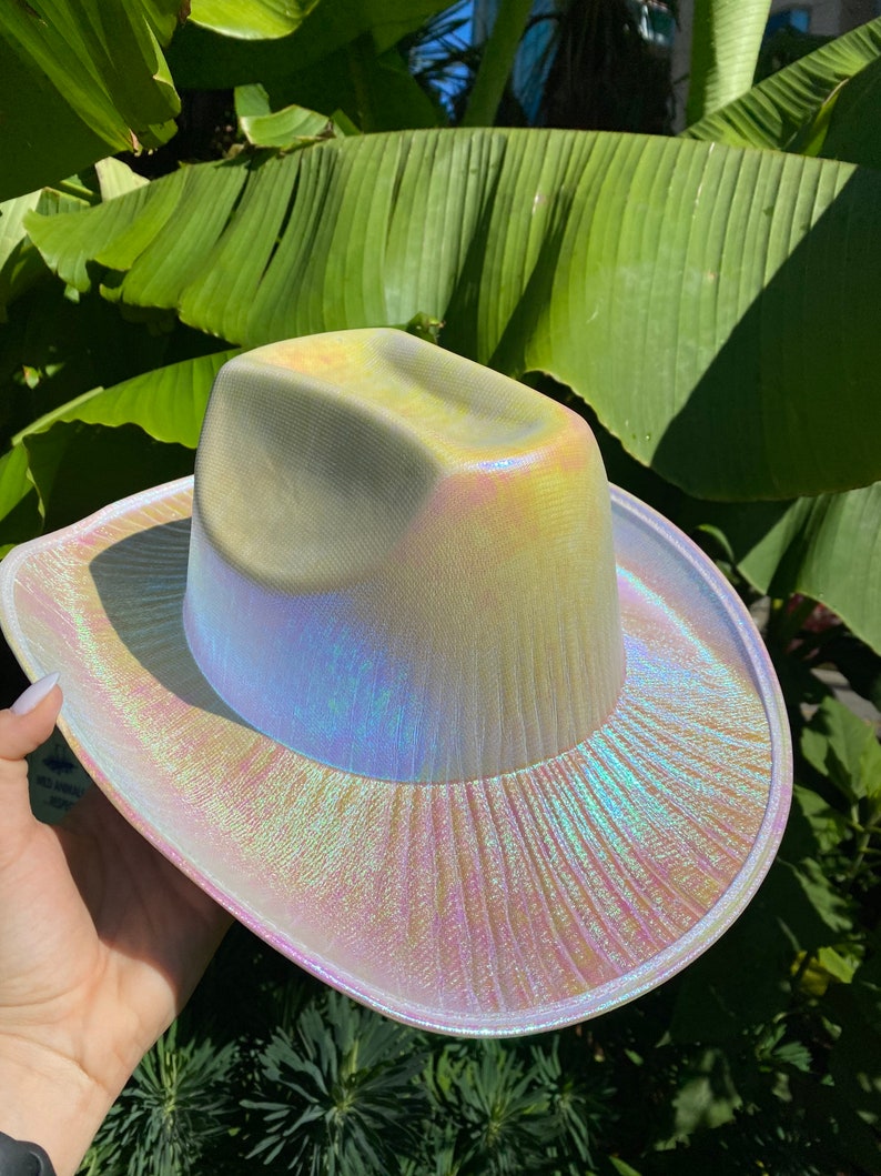 May include: A white iridescent cowboy hat with a wide brim. The hat has a subtle shimmer and a textured surface.