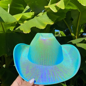 May include: A turquoise iridescent cowboy hat with a wide brim. The hat has a subtle shimmer and a textured surface.