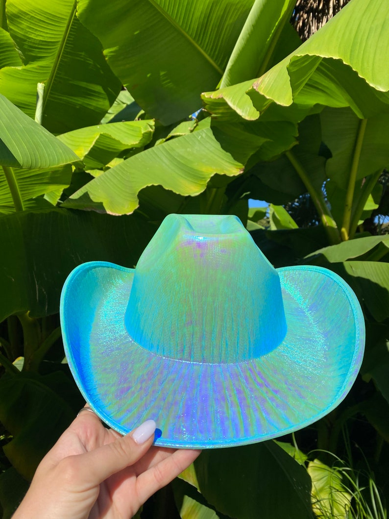 May include: A turquoise iridescent cowboy hat with a wide brim. The hat has a subtle shimmer and a textured surface.