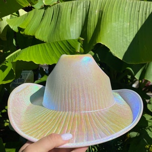 May include: A white iridescent cowboy hat with a wide brim. The hat has a textured surface and a subtle sheen.