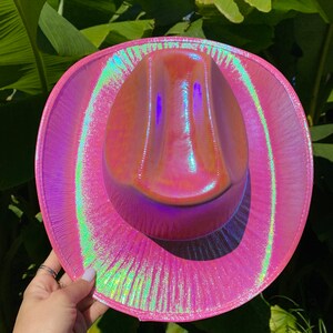 May include: A pink iridescent cowboy hat with a wide brim and a slightly pointed crown.