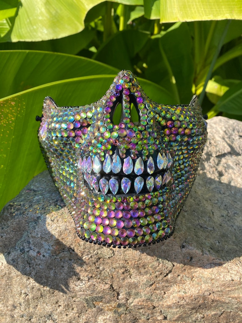 Pu&ograve; includere: Una maschera di teschio nera ricoperta di strass verdi, viola e trasparenti iridescenti.
