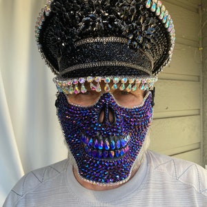 May include: A person wearing a black and silver sequined hat and a blue and black skull mask covered in rhinestones.