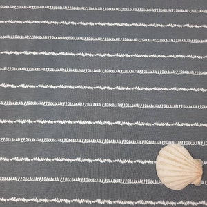 Könnte beinhalten: Grauer Stoff mit weißen wellenförmigen Linien. Eine weiße Muschel liegt auf dem Stoff.