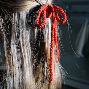 Könnte beinhalten: Ein rotes, flauschiges Haargummi, das zu einem Knoten in den Haaren einer Person gebunden ist.