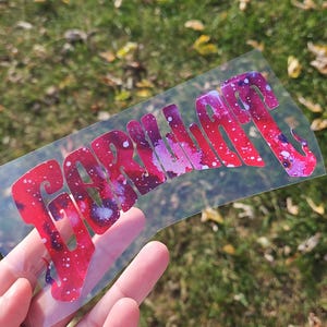 May include: A clear vinyl sticker with the word "GORILLA" printed in a pink and white galaxy design.