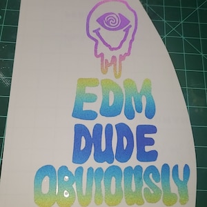 May include: A white sticker with a colorful design. The design features a smiling eye with a spiral pupil, dripping with a rainbow gradient. Below, the words "EDM DUDE OBVIOUSLY" are written in a blue to yellow gradient.