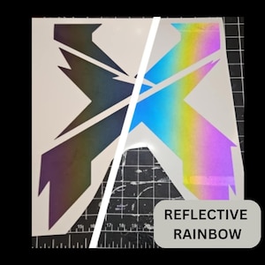 May include: A white sticker with a geometric design, split diagonally. One side is a reflective rainbow, the other is a dark, iridescent color. The text "REFLECTIVE RAINBOW" is in a gray rectangle.