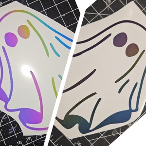 May include: Two iridescent vinyl ghost stickers. The ghost on the left has a rainbow iridescent finish and the ghost on the right has a blue and purple iridescent finish.