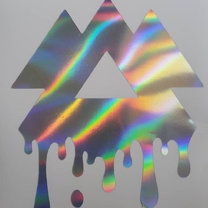May include: Holographic sticker featuring a geometric design of three triangles stacked on top of each other, with a dripping effect at the bottom. The sticker has a rainbow sheen, reflecting various colors. The sticker is on a white background.