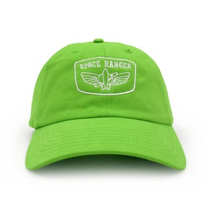 May include: A bright green baseball cap with a curved brim. The cap features a white embroidered patch with the words "SPACE RANGER" and a stylized emblem. The hat is made of a soft fabric and has an adjustable strap.