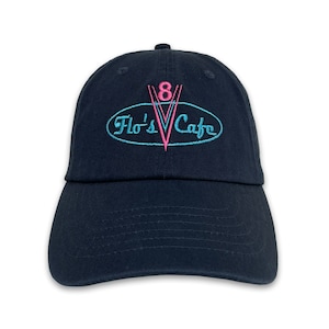 May include: Navy blue baseball cap with the embroidered text "Flo's Cafe" in a retro design. The logo features a pink "8" and a blue oval with the cafe's name. The cap has a curved brim and a button on top.