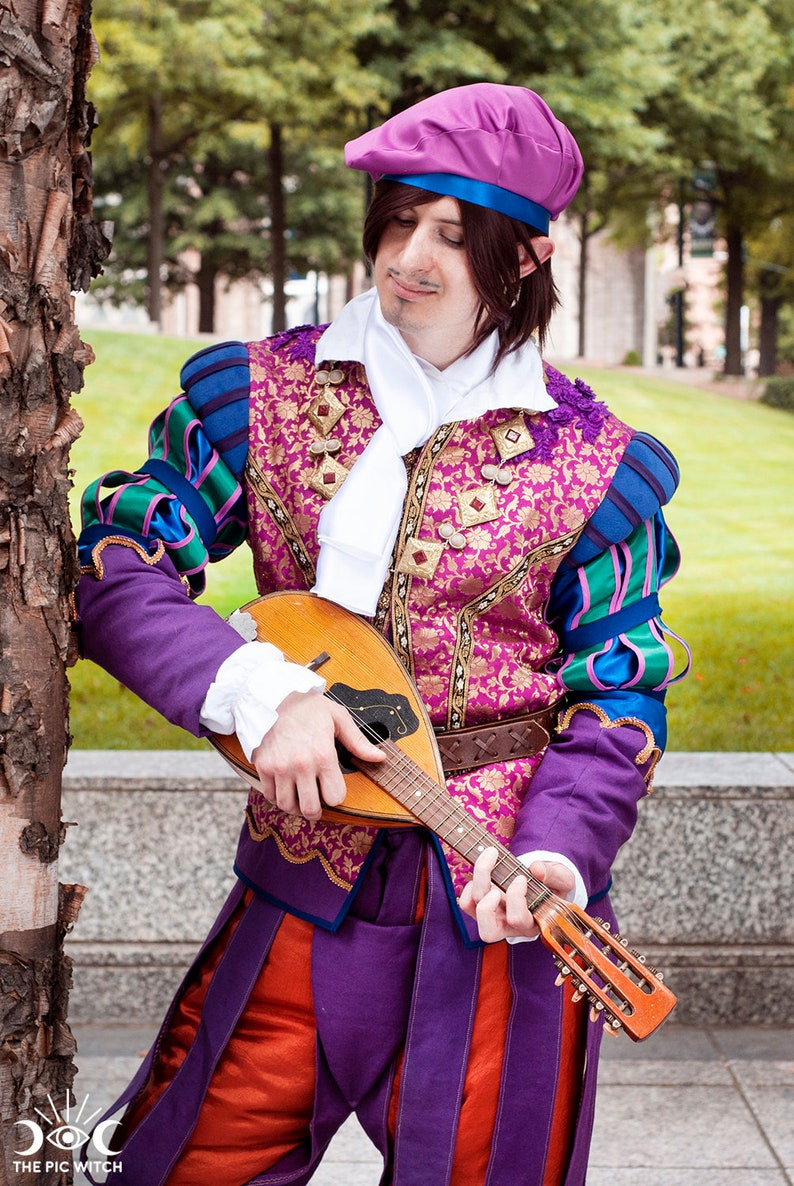 May include: A person wearing a purple and green costume with a purple hat and a white scarf, playing a wooden mandolin.