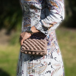 May include: A brown crocheted handbag with a textured design. The bag has a long strap and is worn over the shoulder.
