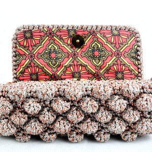 May include: A crocheted clutch purse with a silver and copper metallic yarn. The purse has a geometric patterned lining in shades of red, brown, and yellow.