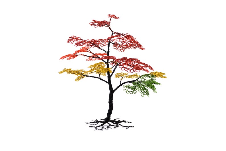 Pu&ograve; includere: Scultura artigianale di un albero in filo di ferro, con tronco e radici neri. Il fogliame passa dal rosso in alto, al giallo e infine al verde in basso, creando un'esposizione colorata. L'albero &egrave; posto su uno sfondo bianco.