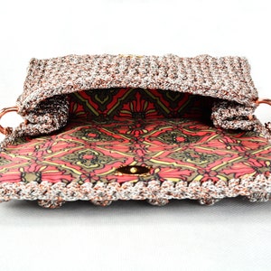 May include: A crocheted handbag with a silver and copper metallic yarn. The bag has a red and green patterned lining and a gold metal clasp.