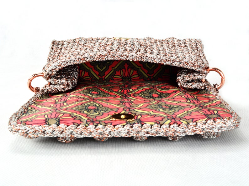 May include: A crocheted handbag with a silver and copper metallic yarn. The bag has a red and green patterned lining and a gold metal clasp.