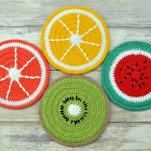 May include: Four crocheted fruit-shaped coasters. The coasters are in the shapes of an orange, a grapefruit, a watermelon, and a kiwi. The coasters are all made with different colored yarn and have a white border.