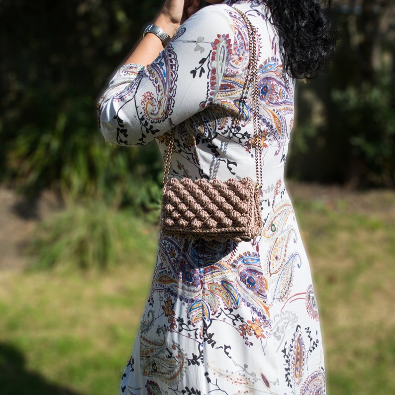 May include: A brown crocheted handbag with a chain strap. The bag has a textured, puffy design.