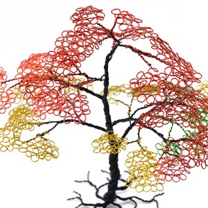 Pu&ograve; includere: Scultura ad albero in filo di ferro fatta a mano con tronco e rami neri. Il fogliame dell'albero presenta anelli di filo rosso, giallo e verde, creando un aspetto colorato e strutturato. La scultura &egrave; ambientata su uno sfondo bianco.