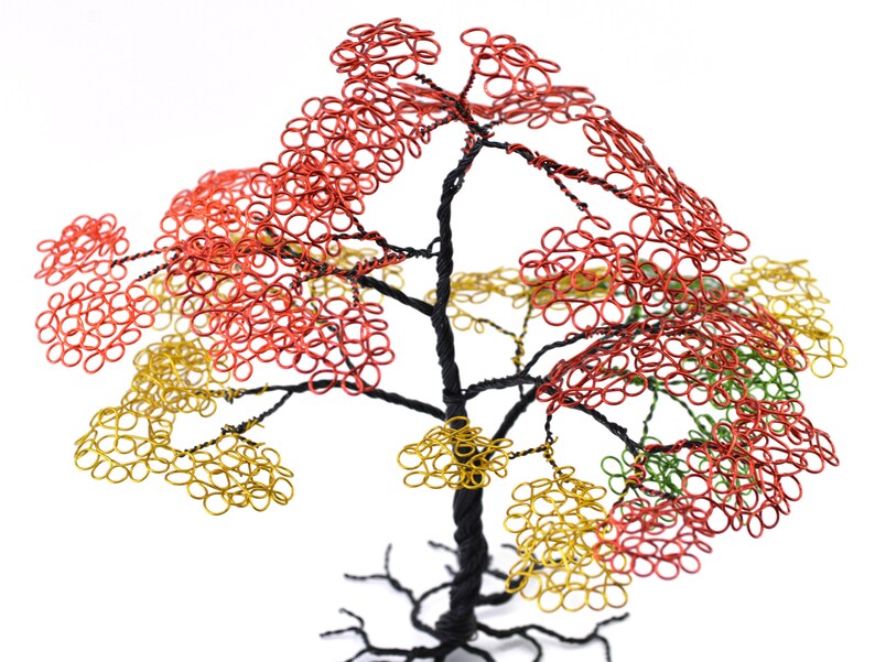 Pu&ograve; includere: Scultura ad albero in filo di ferro fatta a mano con tronco e rami neri. Il fogliame dell'albero presenta anelli di filo rosso, giallo e verde, creando un aspetto colorato e strutturato. La scultura &egrave; ambientata su uno sfondo bianco.