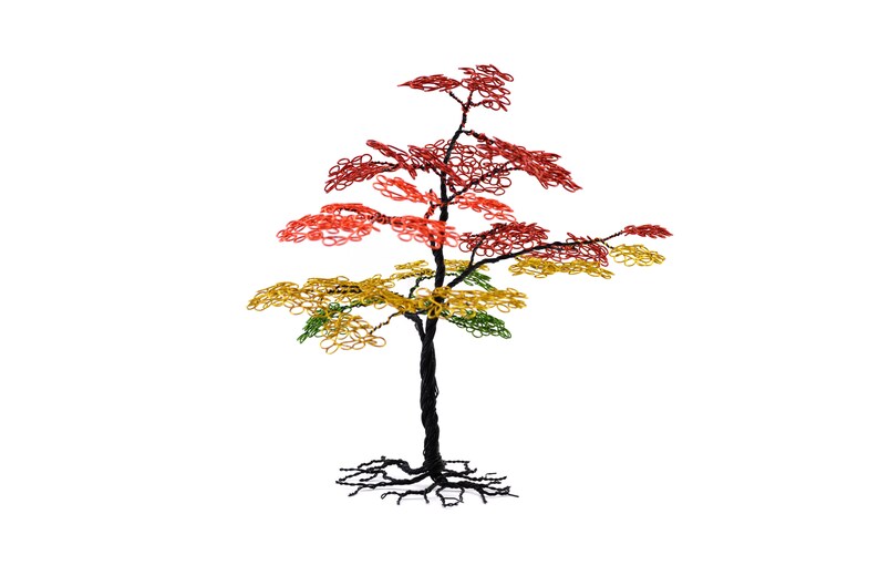 Pu&ograve; includere: Scultura di albero in filo di ferro con tronco e radici neri. Il fogliame dell'albero &egrave; una sfumatura di rosso, giallo e verde. La scultura &egrave; posta su uno sfondo bianco. Un pezzo decorativo.