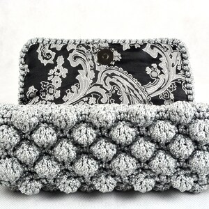 May include: A silver crocheted clutch purse with a black and white paisley fabric lining. The purse has a textured, bubble-like design.