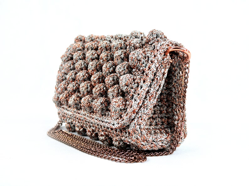 May include: A crocheted handbag with a silver and brown color scheme. The bag has a chain strap and a textured, puffy design.