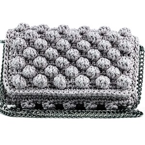 May include: A gray crocheted clutch bag with a silver chain strap. The bag has a textured, bubble-like design.