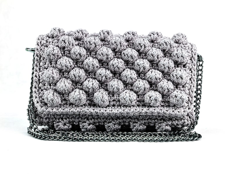 May include: A gray crocheted clutch bag with a silver chain strap. The bag has a textured, bubble-like design.
