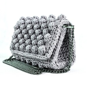 May include: A gray crocheted handbag with a silver chain strap. The bag has a textured, puffy design.